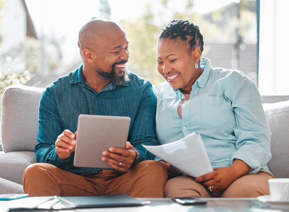 A smiling couple reviewing paperwork and a tablet